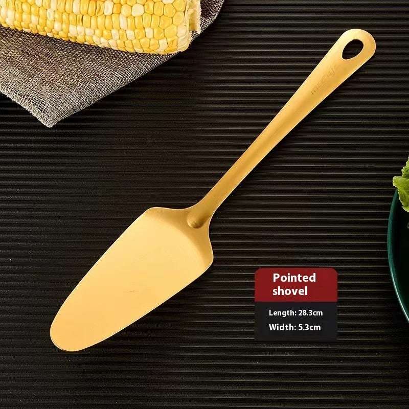 Gold-colored pointed shovel on a dark surface with corn on the cob and a green plant.