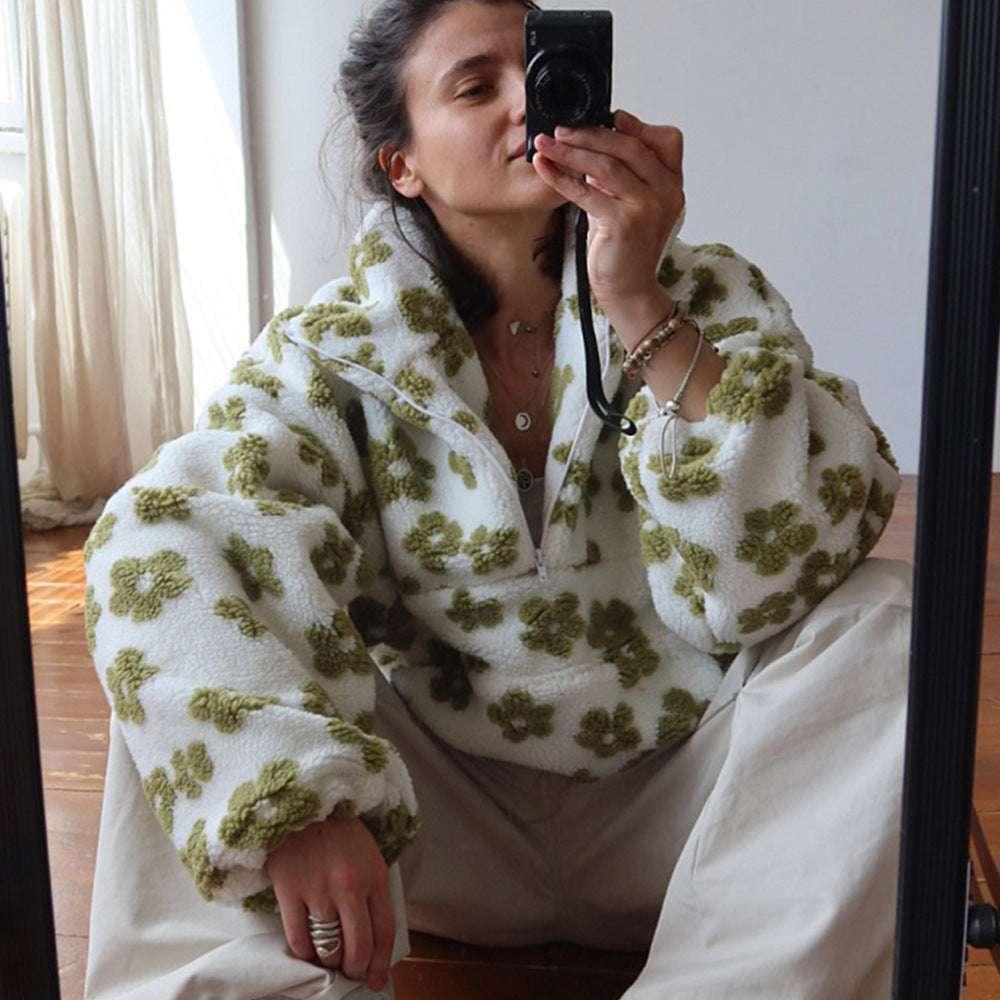 Person wearing a white fleece jacket with green floral patterns, taking a mirror selfie.