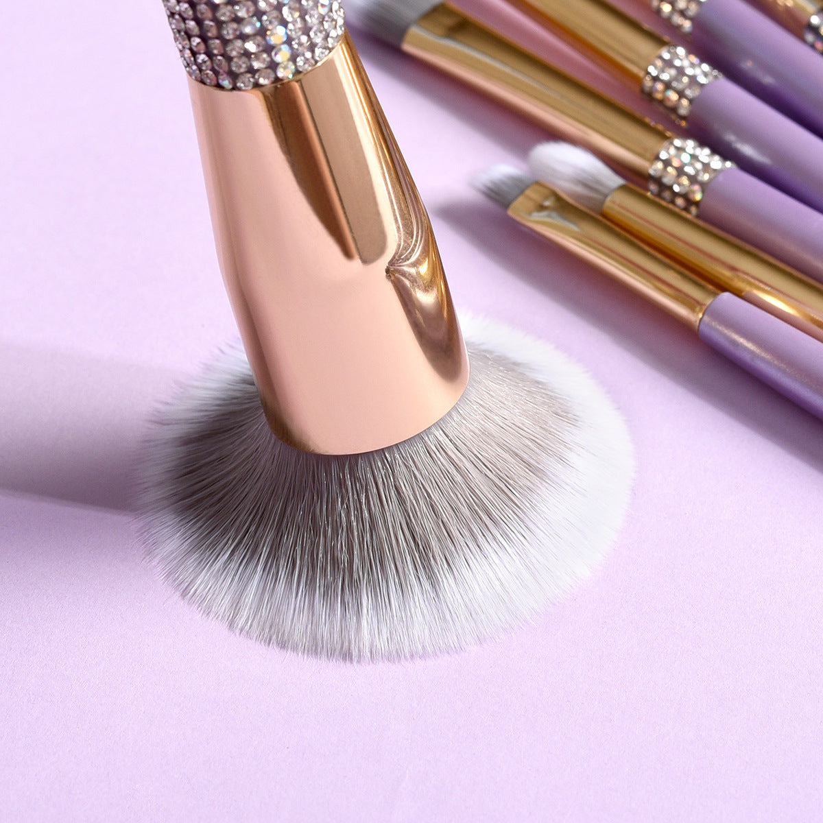 Makeup brushes with rose gold and purple handles on a light purple background