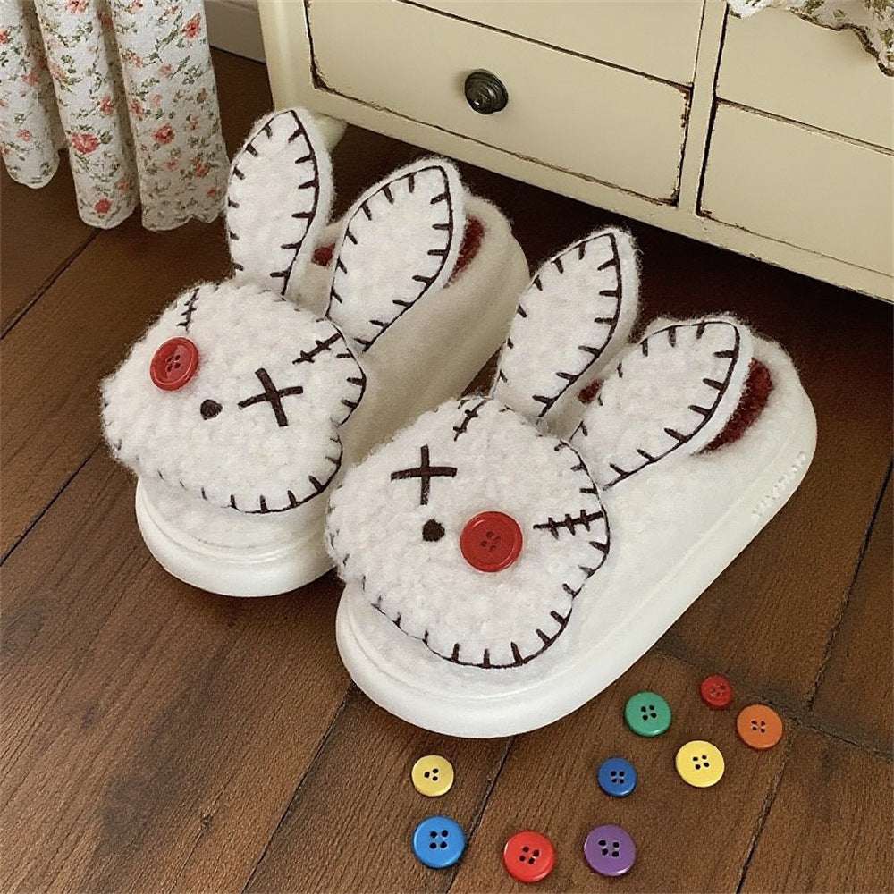 Pair of white bunny slippers with black details and red buttons on a wooden floor.