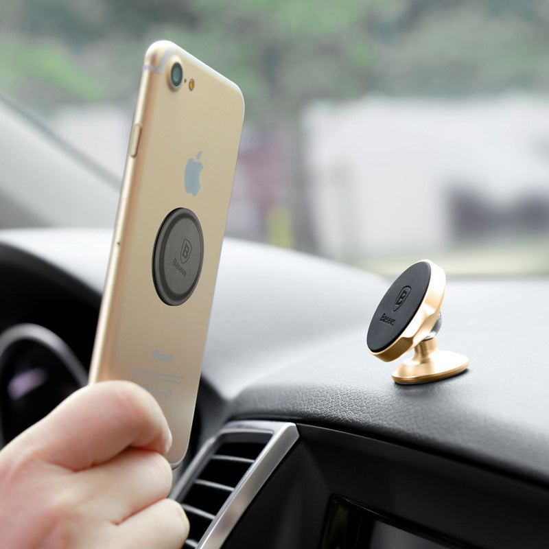 A gold-colored magnetic car phone holder accessory mounted on a car's dashboard with a smartphone attached to it.