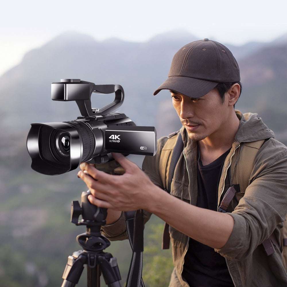 Man holding a 4K camera on a tripod with a mountainous background