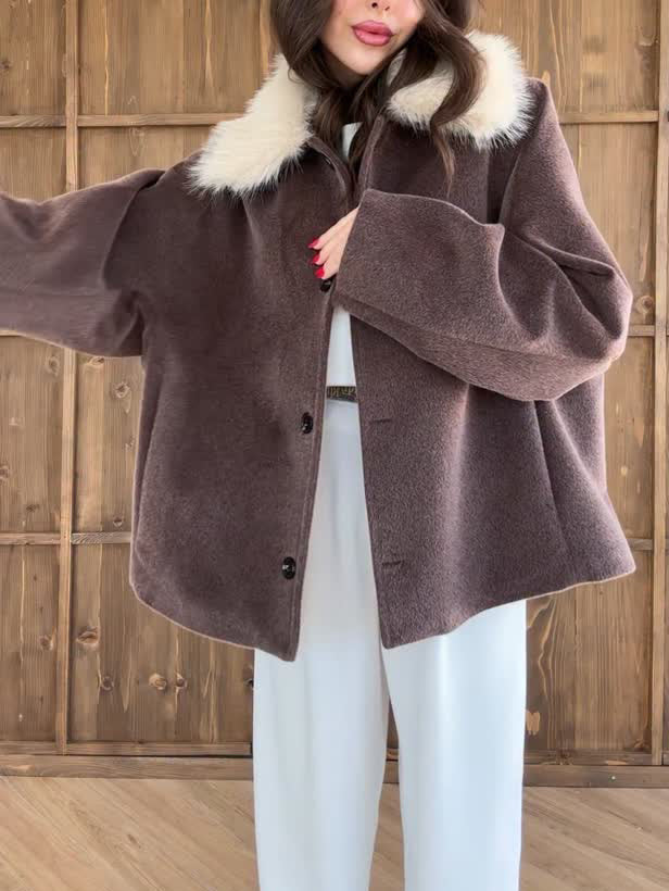 Person wearing a brown coat with fur collar against a wooden background
