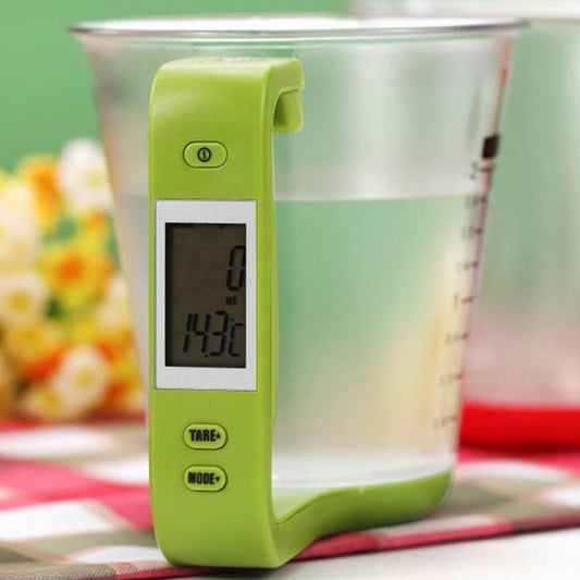 A green electronic scale measuring cup placed inside a clear measuring cup, with an LCD display and buttons visible on the green device.