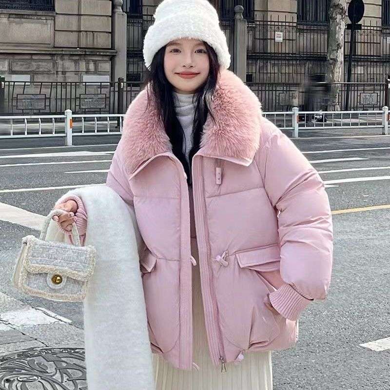 Person wearing a pink puffer coat with a fur-lined hood on a city street.
