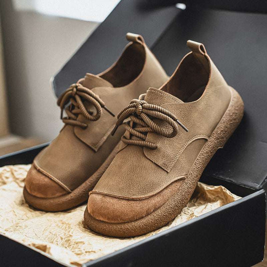 Pair of brown leather shoes with laces on a textured surface