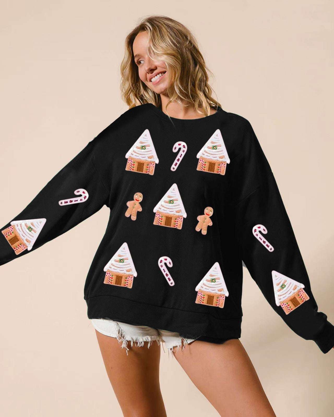 Woman wearing a black sweater with Christmas-themed designs on a beige background