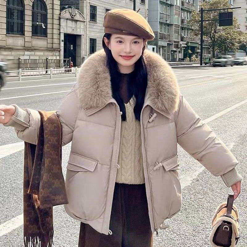 Person wearing a beige puffer jacket with fur collar on a city street.