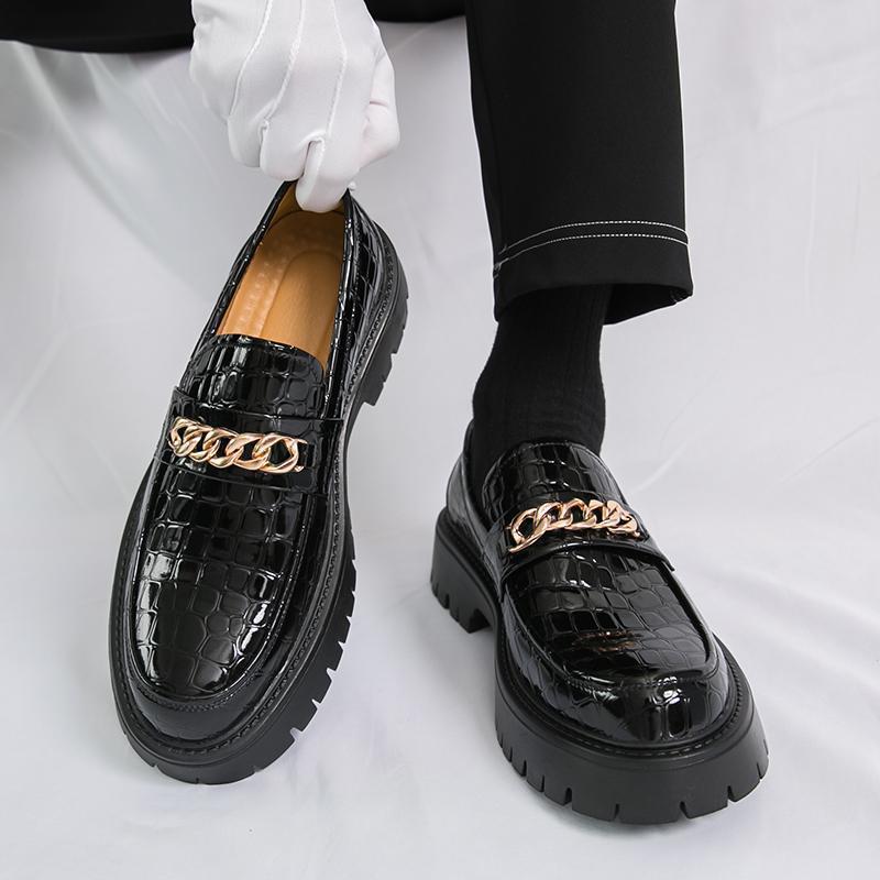 Black crocodile-patterned loafers with gold chain details on a white background