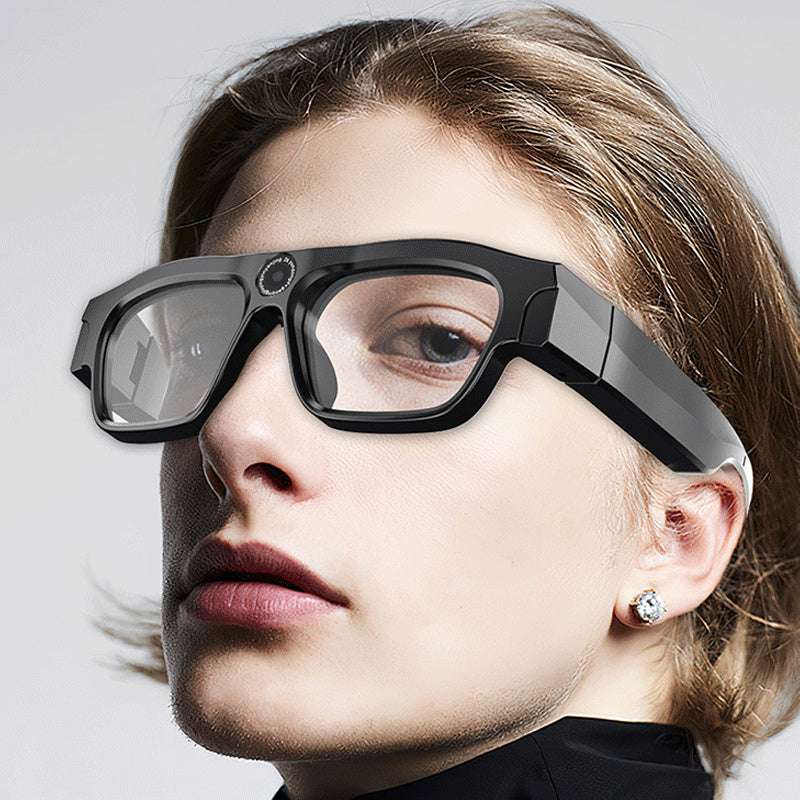 Close-up of a person wearing futuristic black glasses on a plain background