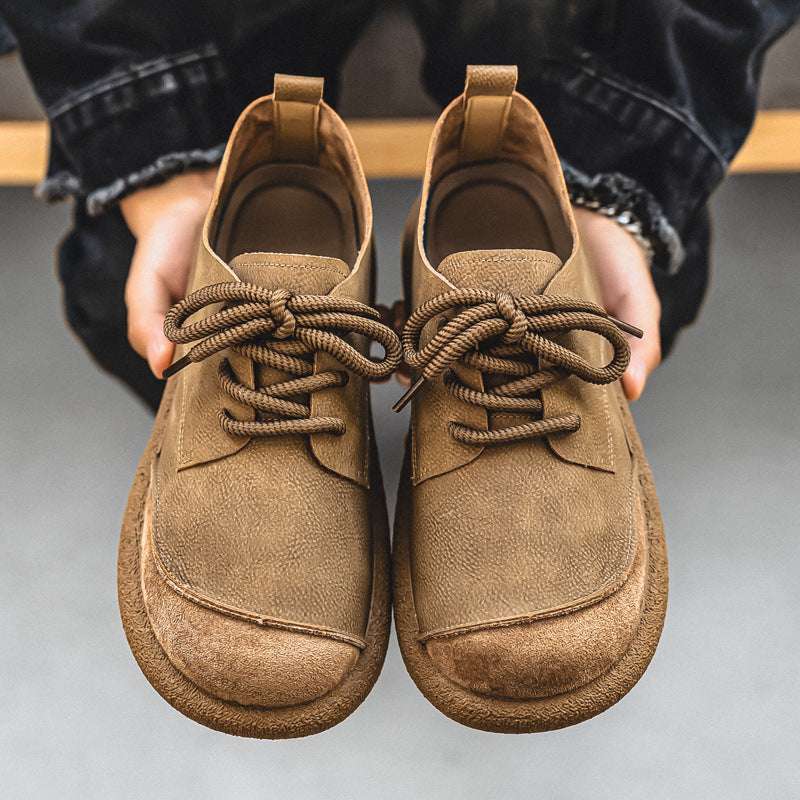 Pair of brown suede shoes held by a person against a neutral background