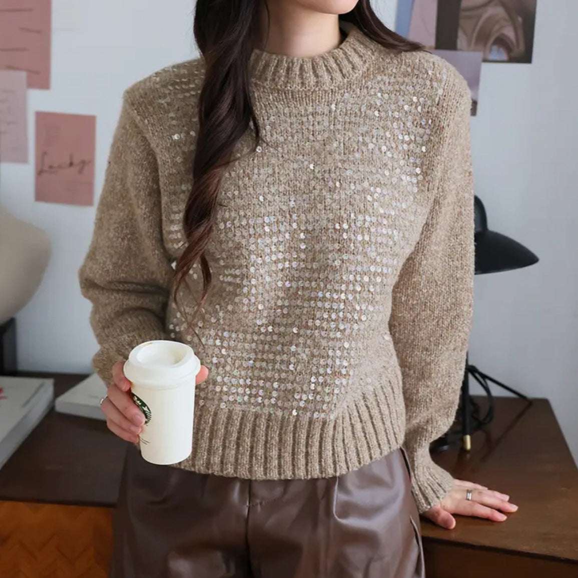 Person wearing a beige sequin sweater holding a Starbucks cup indoors.
