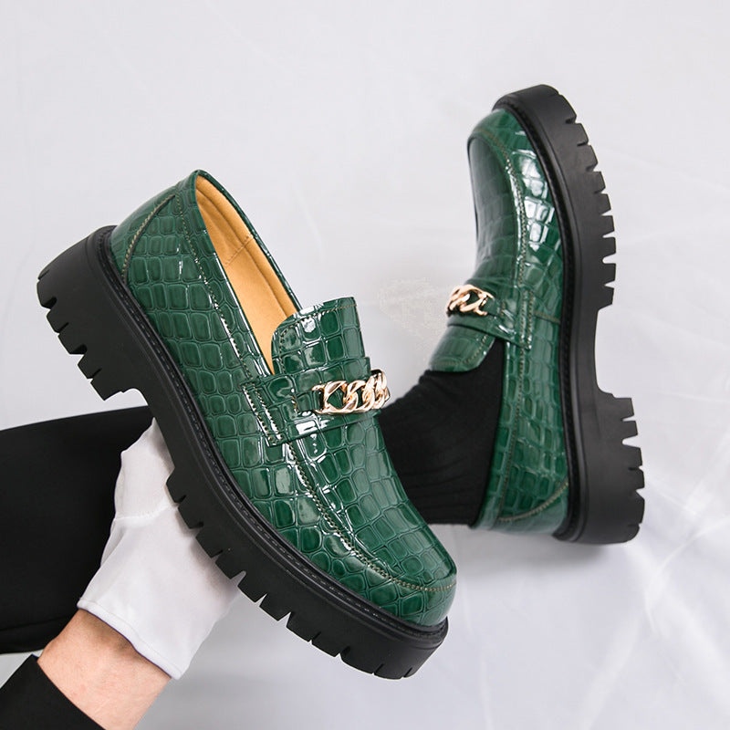 Green crocodile-patterned loafers with gold chain detail on a light gray background