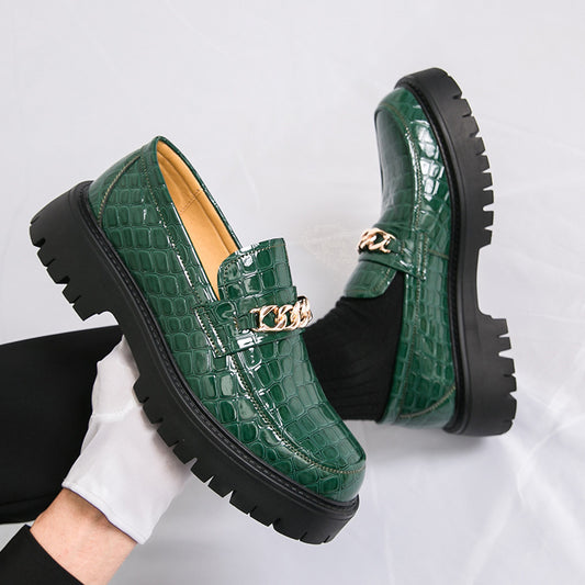 Green crocodile-patterned loafers with gold chain detail on a light gray background