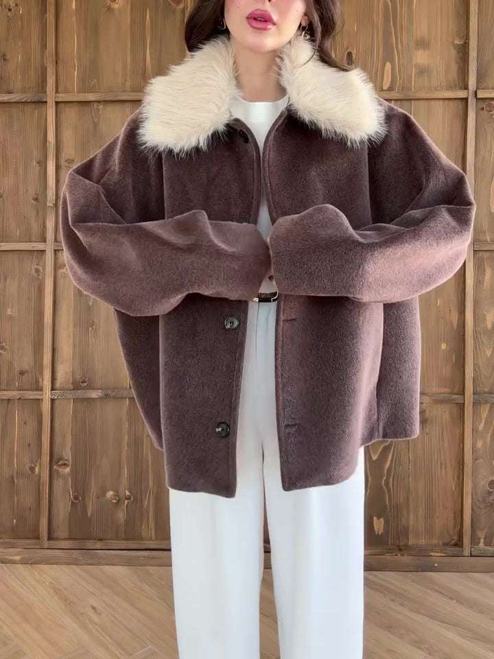 Person wearing a brown coat with a fur collar against a wooden background
