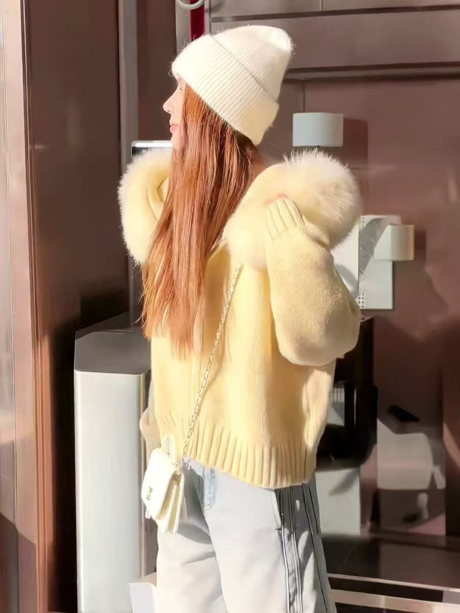 Person wearing a yellow fur-lined coat and white beanie inside a building.
