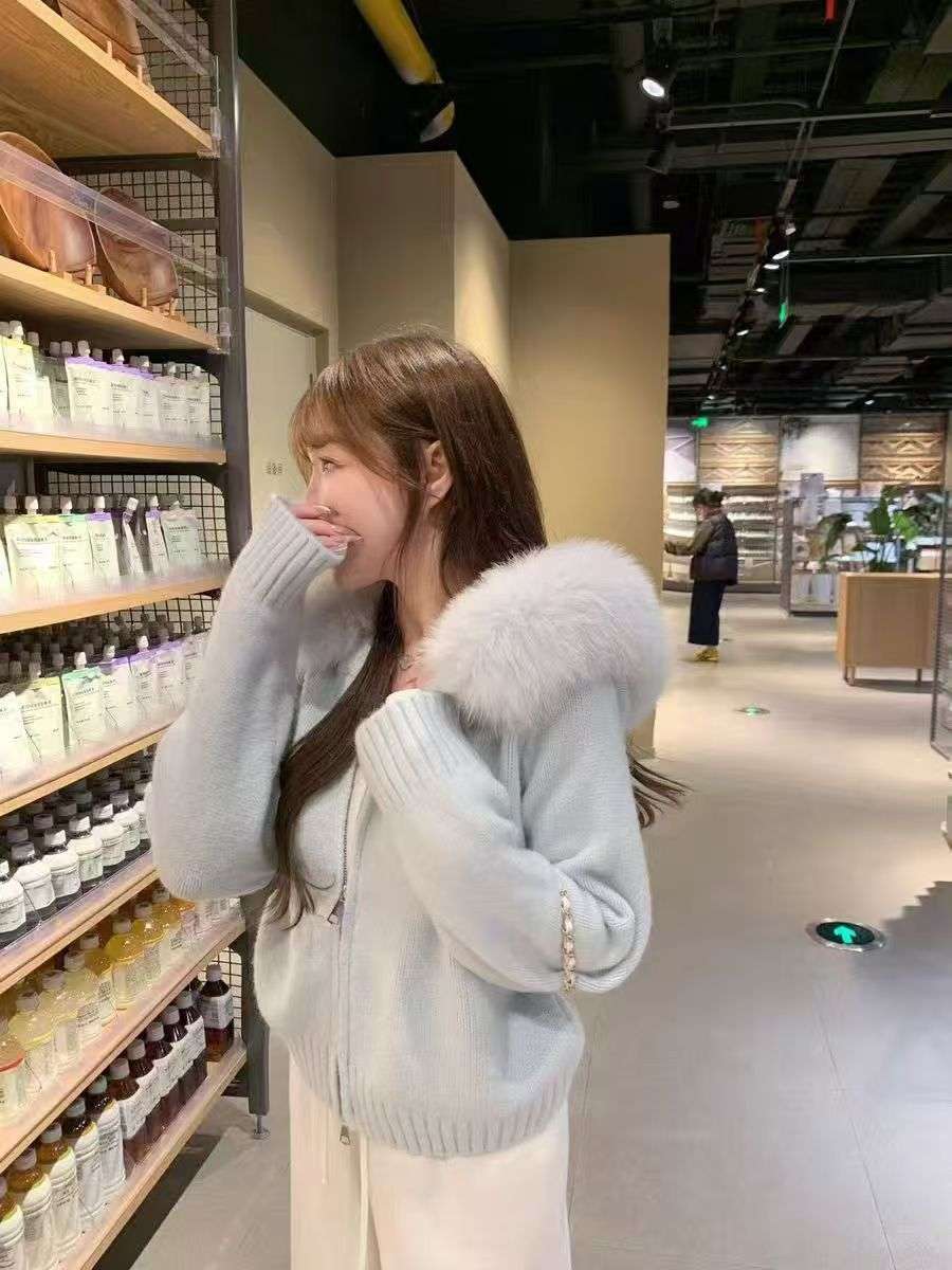 Woman wearing a light blue sweater with a fur-lined hood in a store setting.