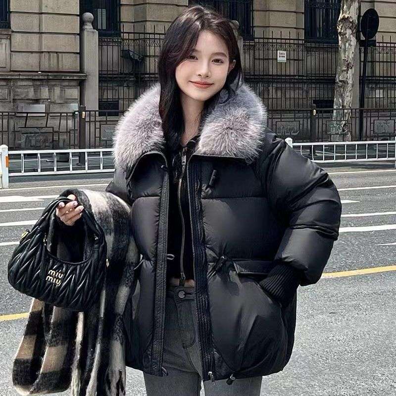 Woman wearing a black puffer jacket with fur collar on a city street.