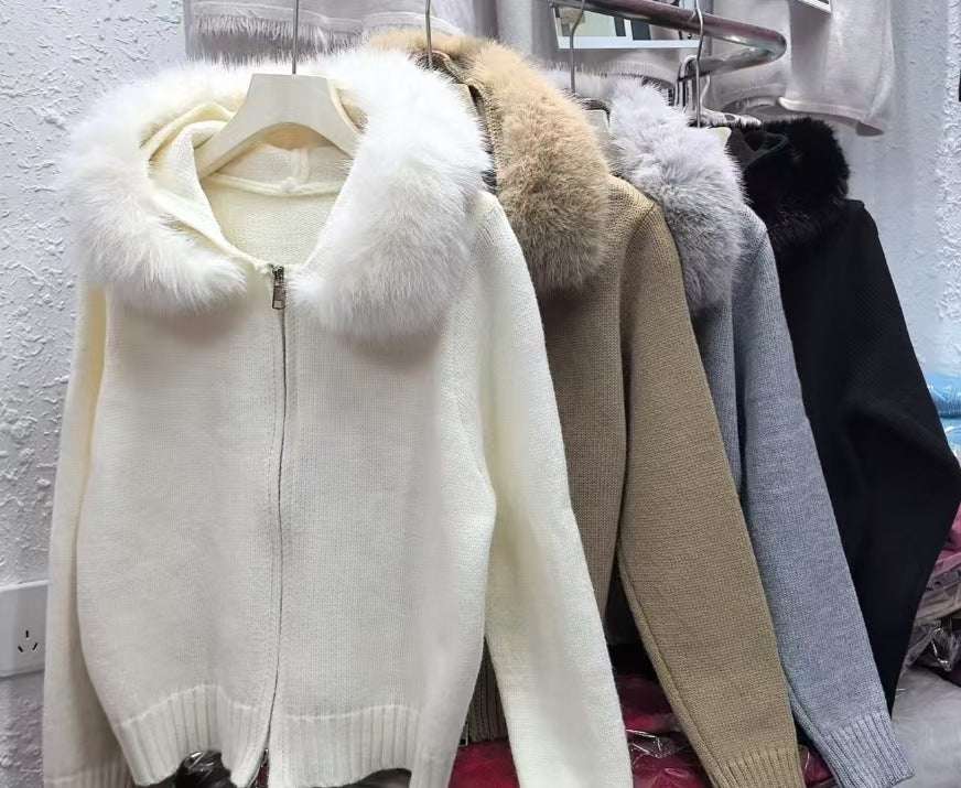 White sweater with fur hood on a hanger against a white wall.