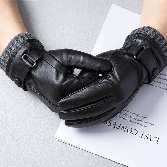 Black leather gloves worn by a person on a light gray surface with a book underneath.