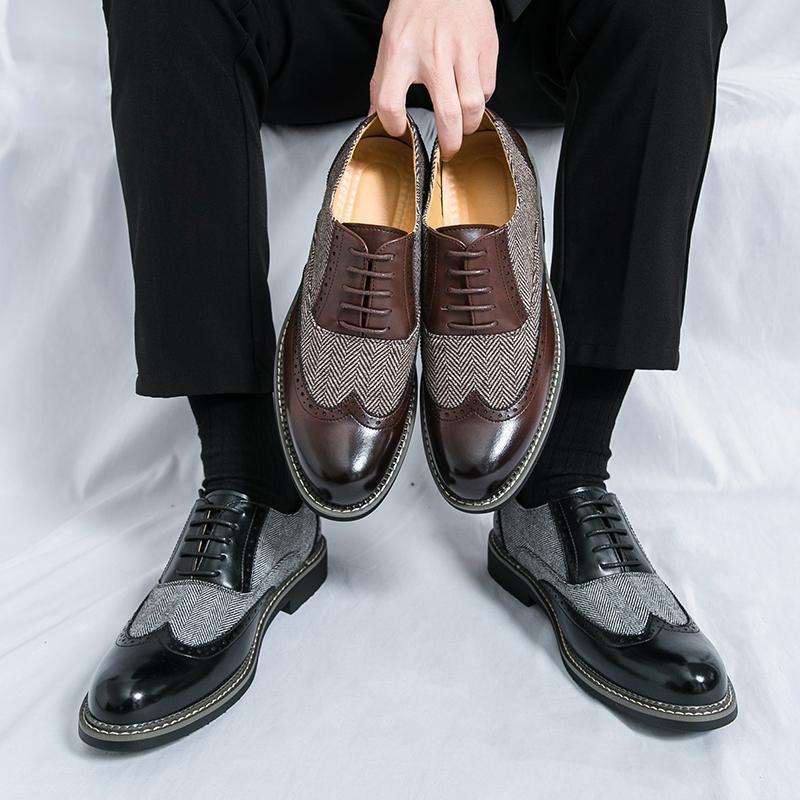 Person holding a pair of brown and gray dress shoes against a white background