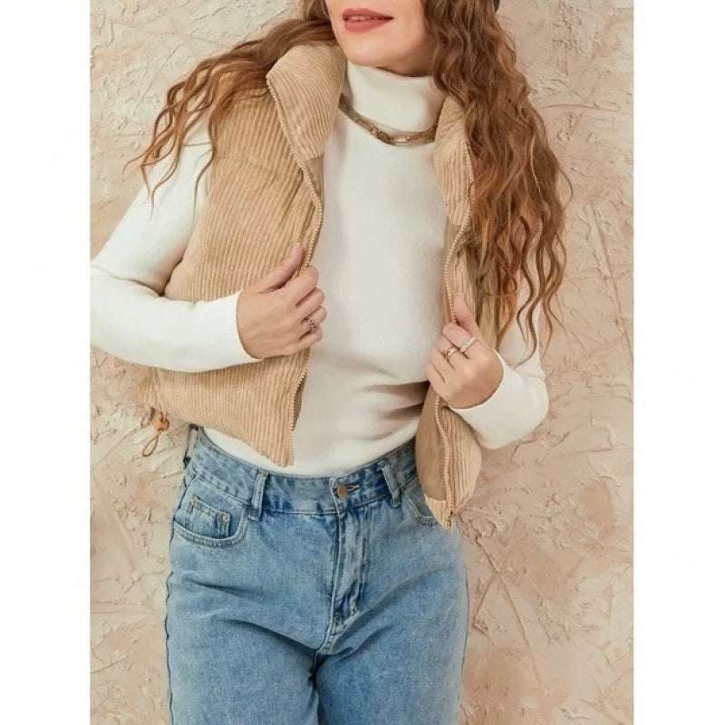 Woman wearing a beige vest over a white turtleneck and blue jeans against a beige background