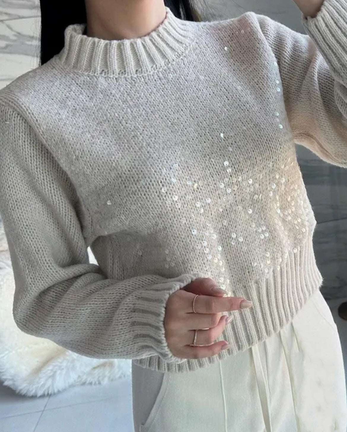 Close-up of a person wearing a light gray sweater with pearl embellishments.