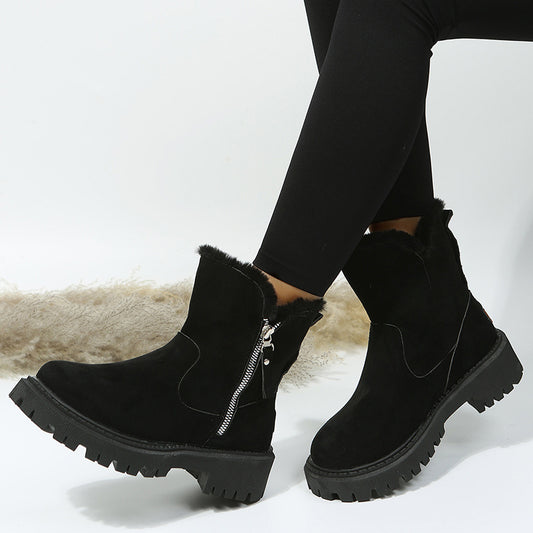 Black suede ankle boots with fur lining and zippers worn by a person on a light background