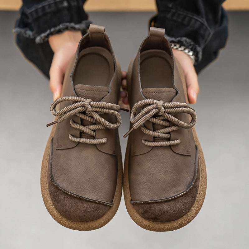 Pair of brown leather shoes held by a person on a neutral background