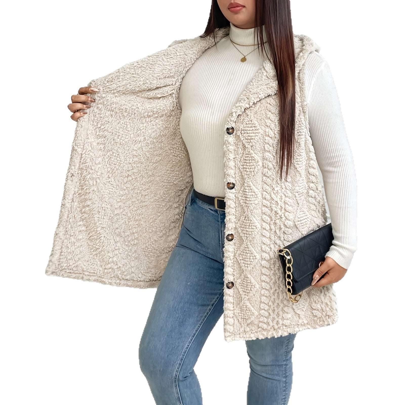 Woman wearing a beige knitted cardigan over a white turtleneck and blue jeans, holding a black clutch.