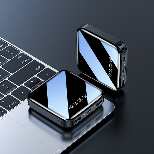 Two portable power banks with mirrored surfaces, one standing vertically displaying charging status, the other lying horizontally; both on a dark background next to a keyboard.