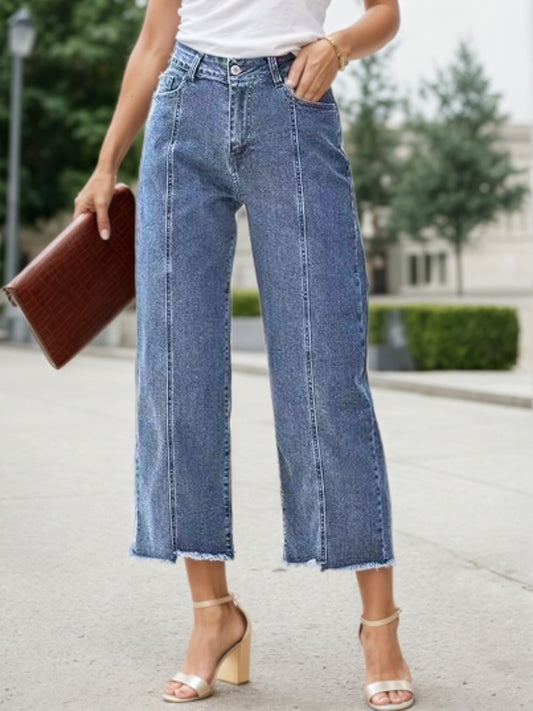 A plus-size model wearing high-waisted wide-leg denim pants with a 7-inch straight-leg hem, styled with a tucked-in blouse for a fashionable casual look.