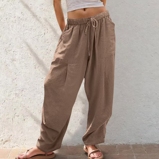 A woman lounging in sage green cotton-linen blend pants featuring a relaxed straight-leg cut, side pockets, and a functional drawstring waistband.