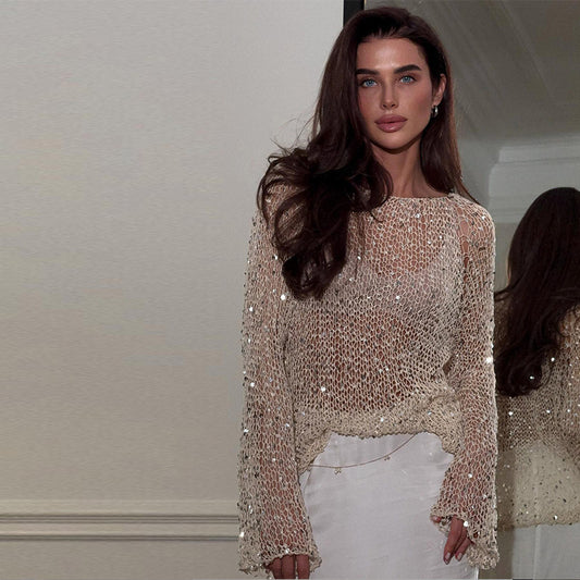 A woman modeling a loose-fitting, long-sleeved knitted top with intricate hollow-out patterns and shimmering sequin accents throughout the knit.