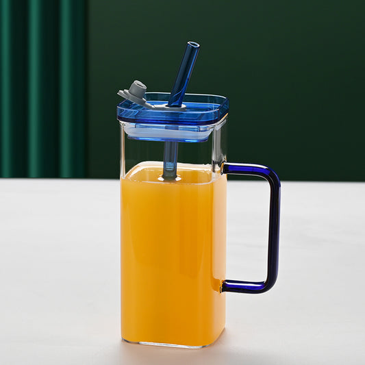 Elegant blue-tinted square glass cup with a clear glass straw and lid, filled with a refreshing cold drink on a minimalist desk