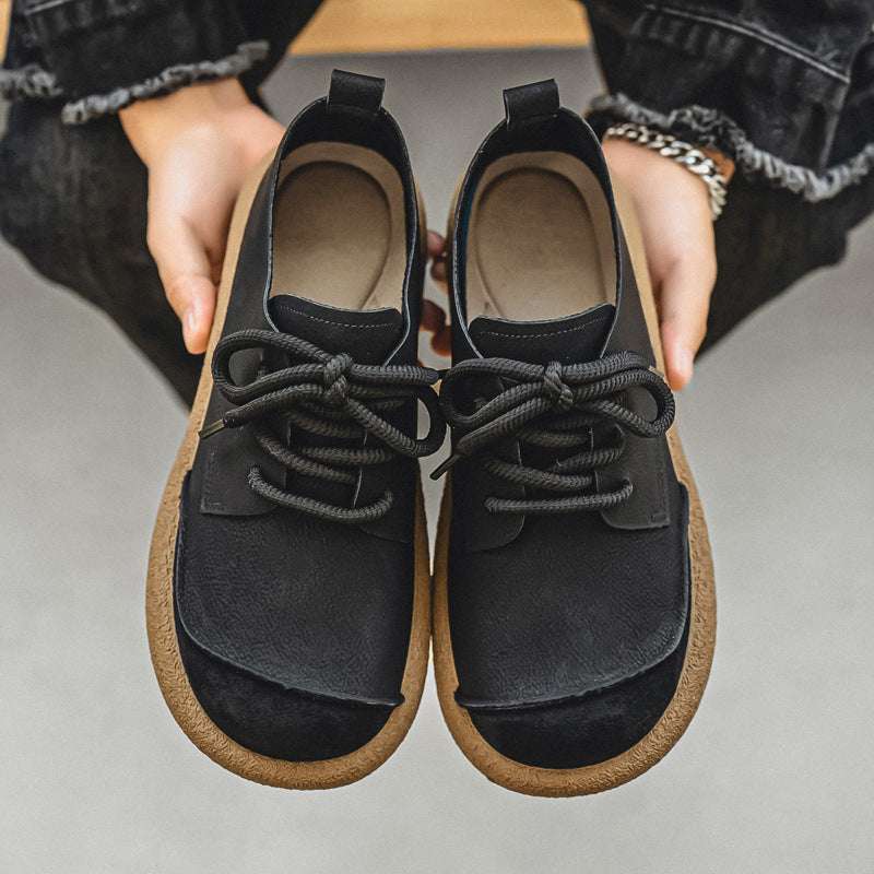 Black and brown shoes held by a person on a neutral background