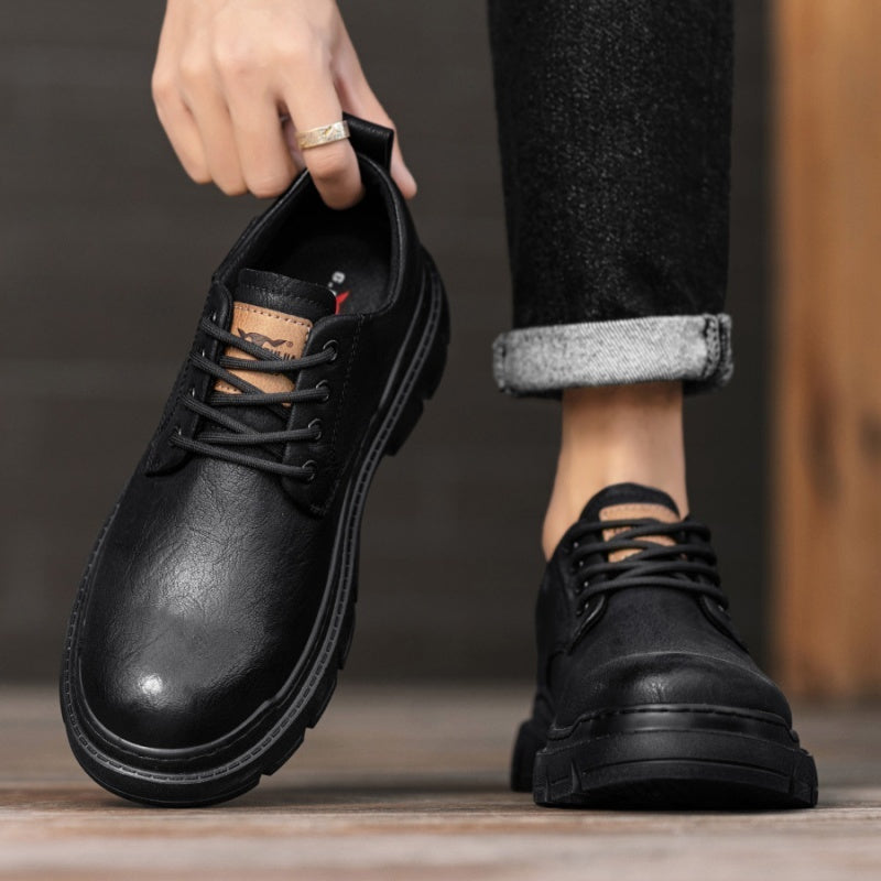 Person holding a black leather shoe with another black leather shoe on a wooden floor.