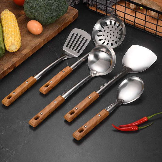 Set of kitchen utensils with wooden handles on a dark surface with vegetables in the background.