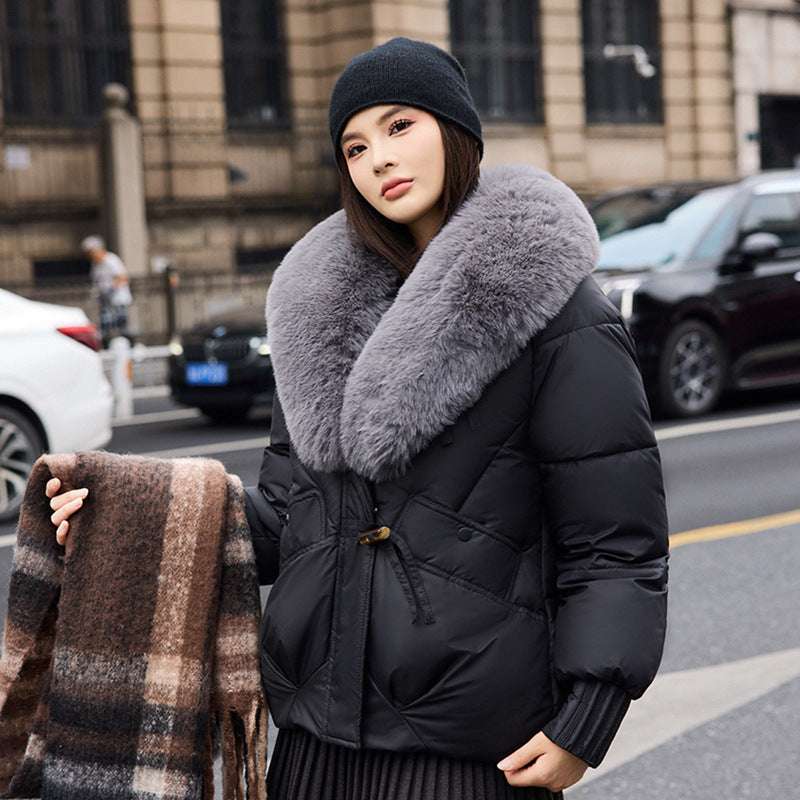 Woman wearing a black coat with a large fur collar on a city street.