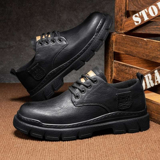 Black leather shoes with thick soles on a textured surface with wooden crates in the background.