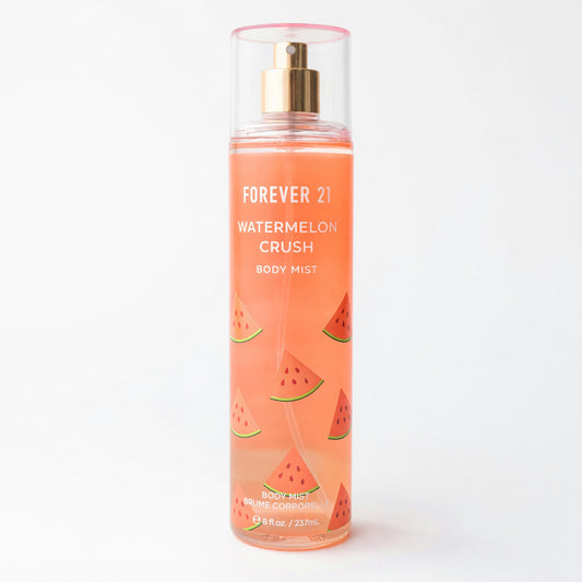Watermelon Crush body mist bottle with gold pump, clear cylinder, pink-orange liquid.