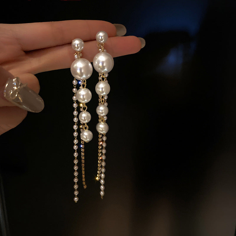 Pearl earrings with gold accents held by a hand against a dark background