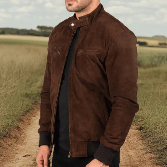 Man wearing a brown jacket standing on a dirt path with a field in the background