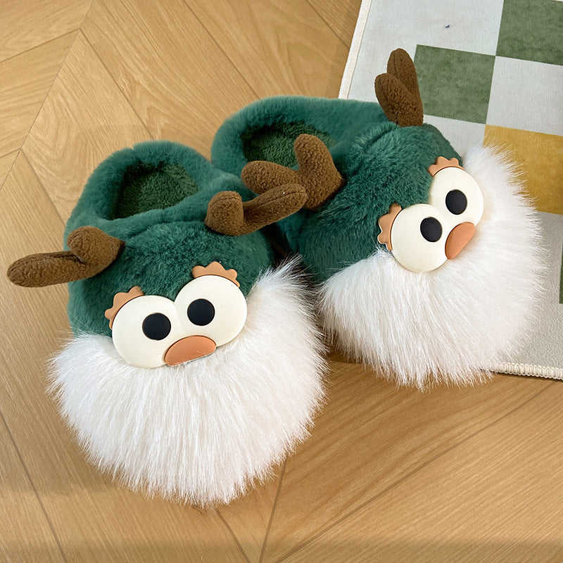 A pair of green plush slippers designed to resemble cartoon deer with white fur around the edge and brown antlers, placed on a wooden floor.