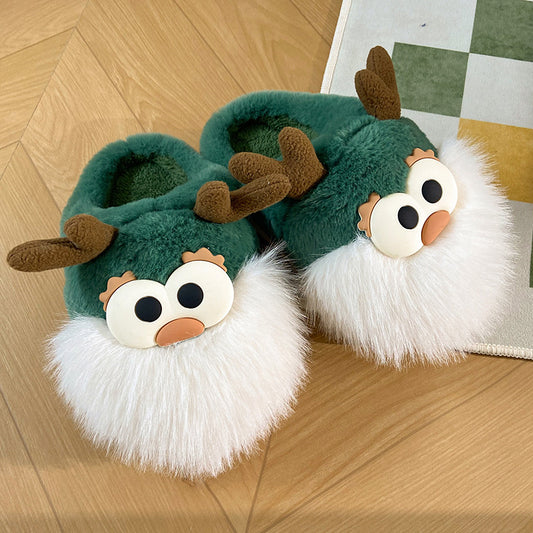 A pair of green plush slippers designed to resemble cartoon deer with white fur around the edge and brown antlers, placed on a wooden floor.