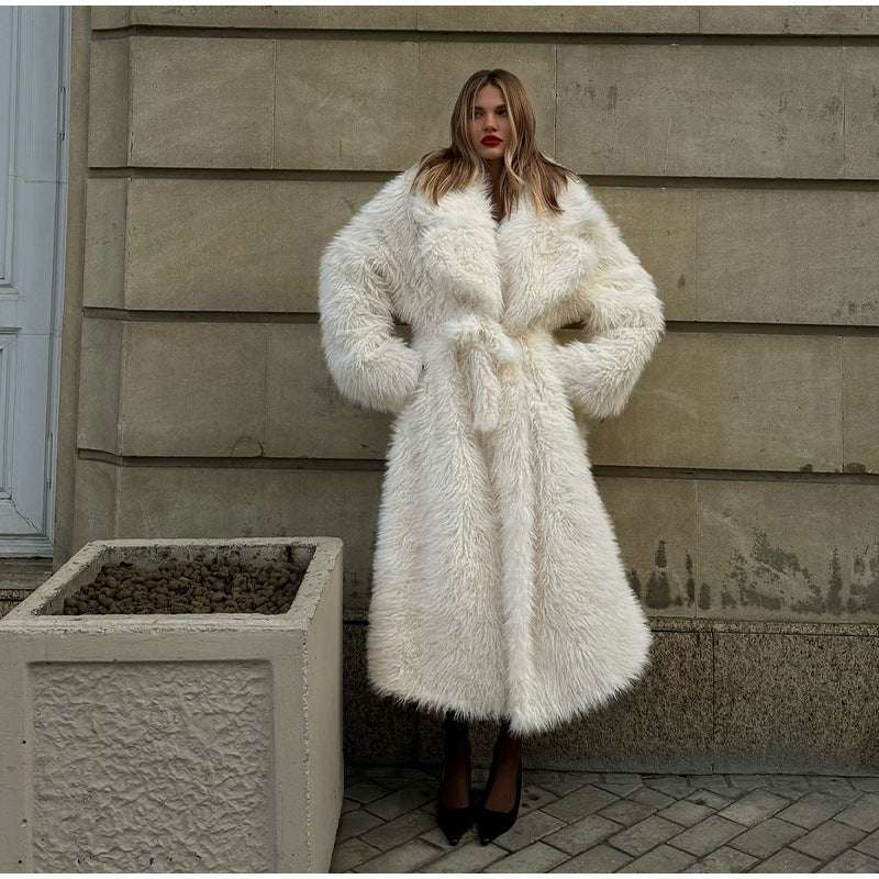 Woman wearing a white fur coat standing against a beige wall.