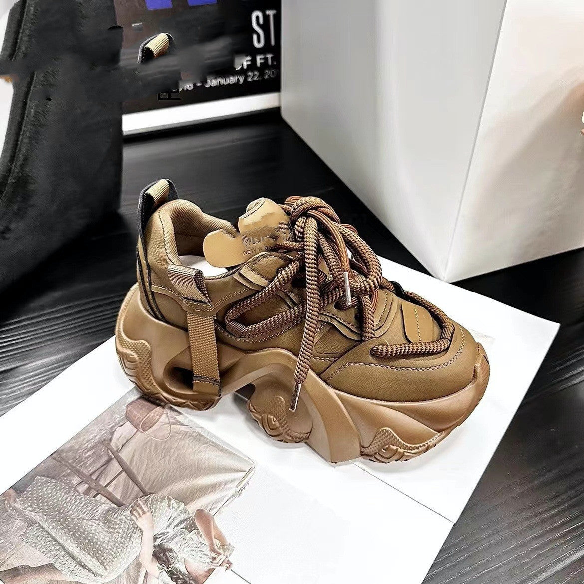 A pair of women's sneakers with thick soles and lace-up closure, displayed in a store setting, with one sneaker in brown color and the other in black color.