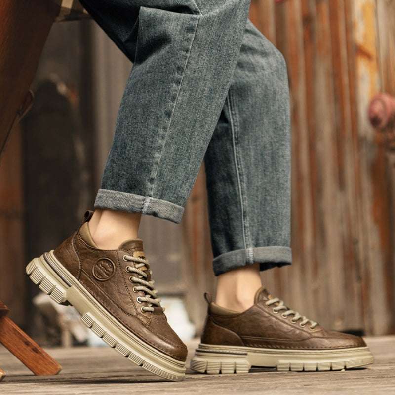 Brown leather shoes with white soles worn with rolled-up jeans on a wooden floor.
