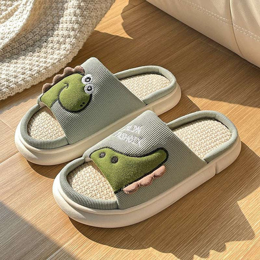 A pair of green dinosaur-shaped slippers with a cartoonish design, placed on a wooden floor.