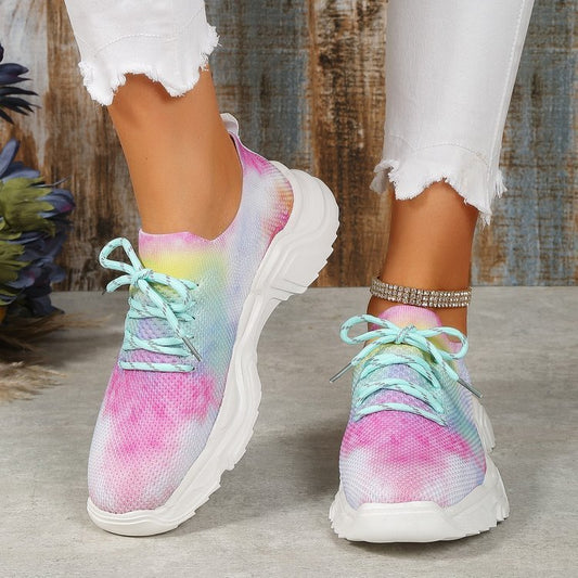 A pair of women's casual sports shoes with a multicolored floral pattern on the upper mesh and a white flat sole.
